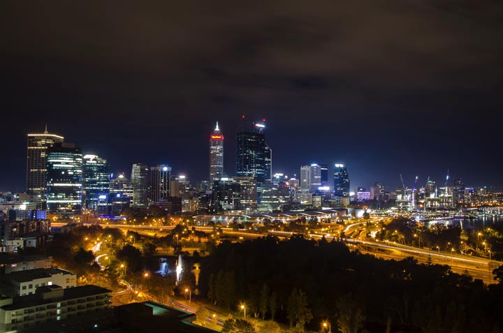 Time lapse image of the Perth CBD at night. Showing the Perth skyline against a nearly clear, deep purple sky. The business towers all with many lights on, and the roads with an orange glow.